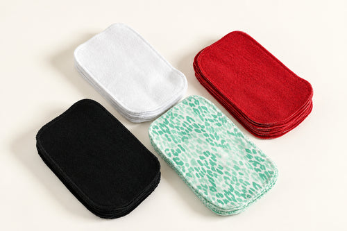 Quatre piles de feuillets hygiéniques réutilisables ; une blanche, une noire, une rouge et une à motifs vert et blanc. 