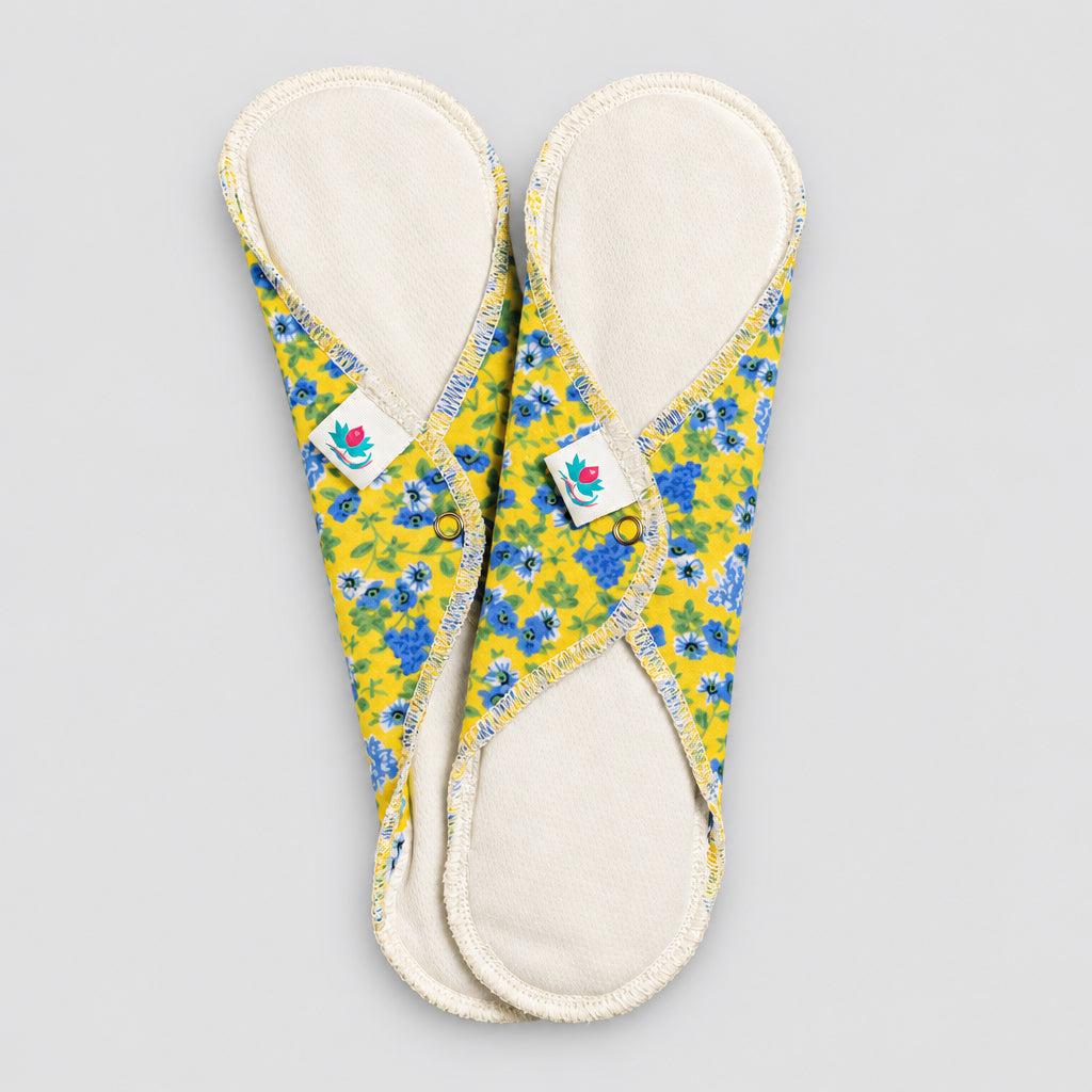 Deux serviettes hygiéniques entretien facile dessus blanc et dessous jaune et fleurs bleues.