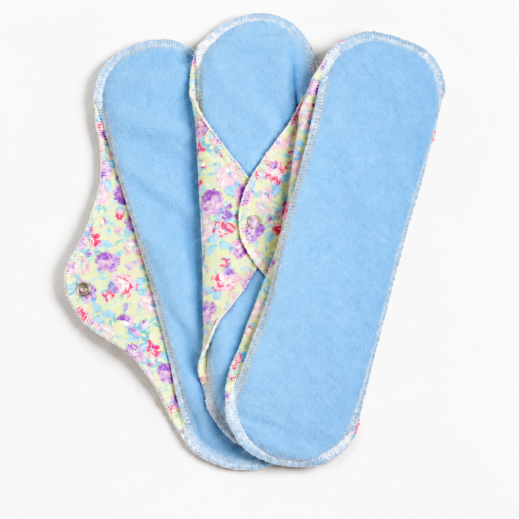 Serviettes hygiéniques avec micropolar bleu ciel sur le dessus et flanelle de coton fleuri dans les tons de vert tendre, mauve et rose en-dessous.