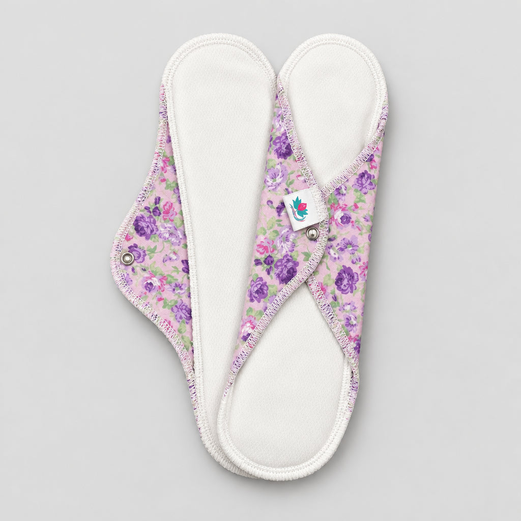 Deux serviettes hygiéniques entretien facile dessus blanc et dessous mauve avec fleurs roses, violettes.